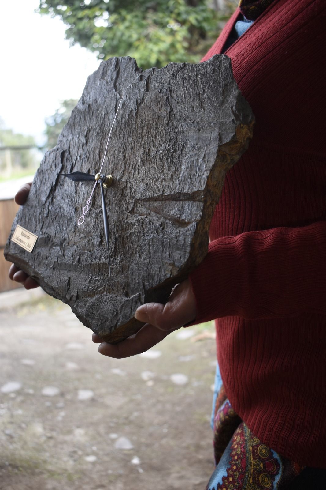 Reloj de pared en una laja de piedra oscura sostenido por unas manos.
